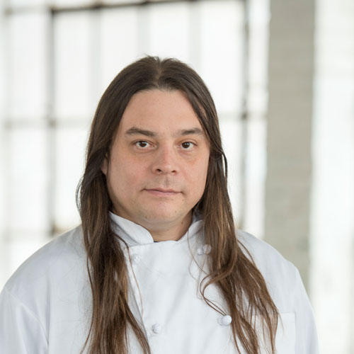 Man with long hair wearing a white chef's jacket.