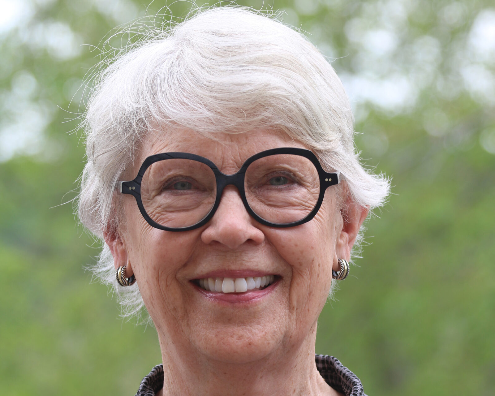 Woman with short white hair and glasses smiling into the camera.