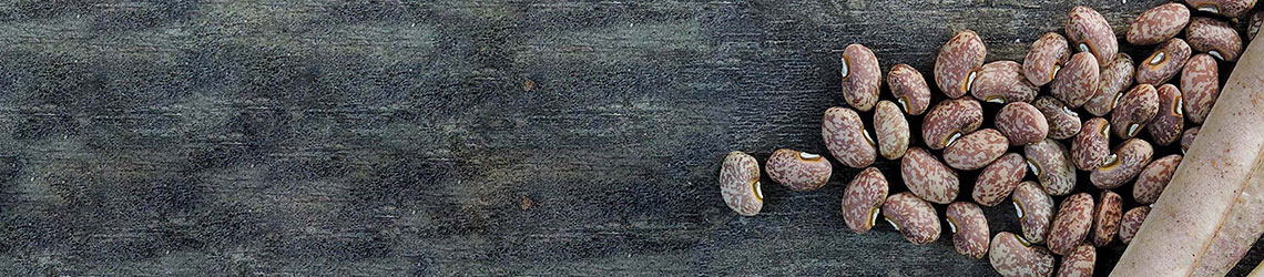 A small group of brown and white speckled beans over a dark gray wood surface