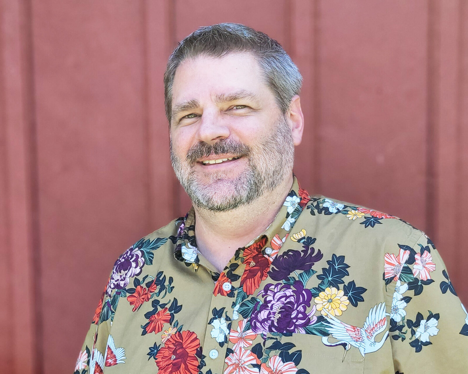 Man wearing a floral print button-down shirt smiles into camera.