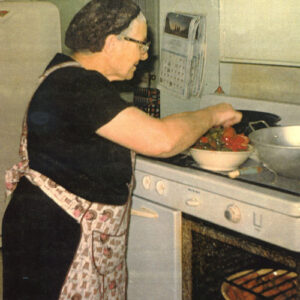 A woman in an apron cooks tomatoes on a stove top