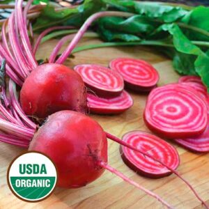 Two whole red beets with stems and leaves, with several round beet slices on a wood surface