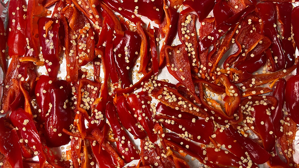 Many small red peppers, halved covered in seeds, laid out on a metal sheet