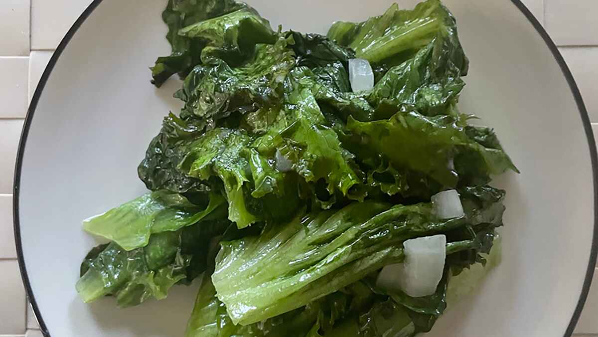 A pile of wet and slightly wilted greens with chopped white onion pieces on a white plate