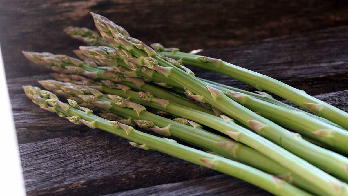 A pile of asparagus lies on a wooden surface