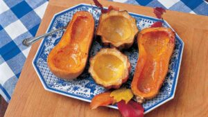 A decorative blue and white plate with four squash halves and fall leaves, on top of a wooden surface and a blue and white plaid cloth