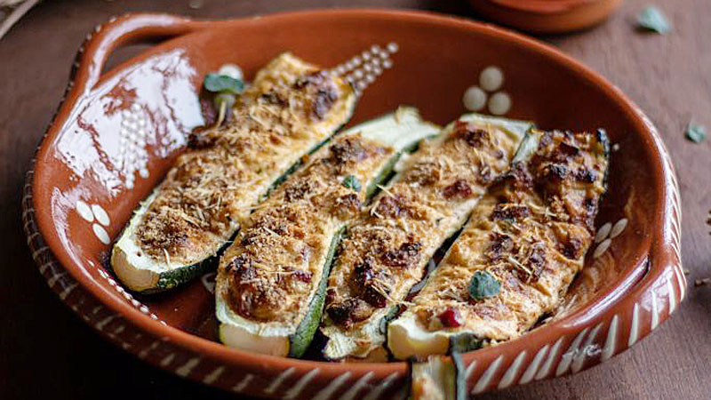 Four zucchini halves stuffed with meat and cheese in an orange bowl