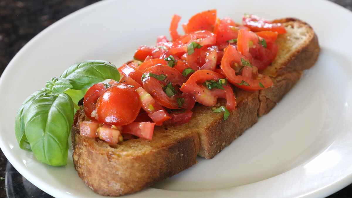 Chopped tomatoes with basil leaves on top of a long slice of bread on a white plate