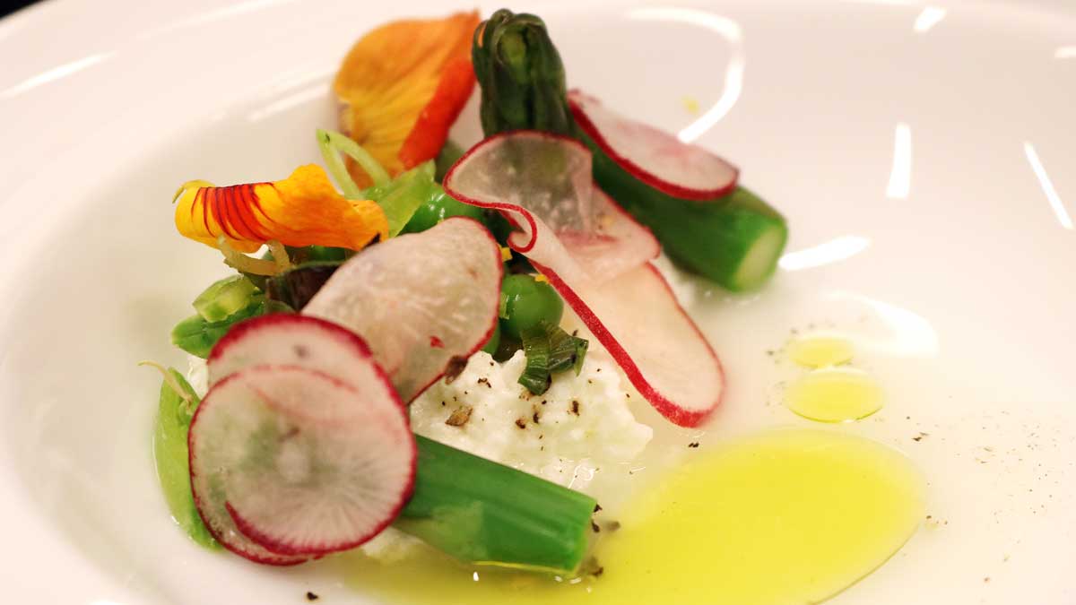 Thin, red and white radish slices on a white plate with small green vegetable pieces and yellow oil