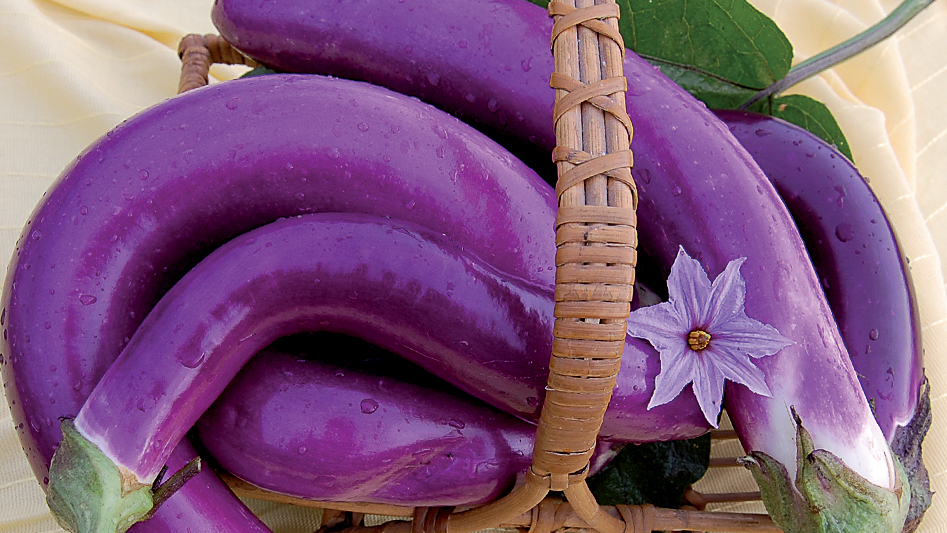 A basket of long purple eggplant with a purple flower