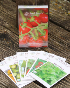 One packet with tomatoes which says Seed Savers Exchange Salsa Collection, with 6 packets of various seeds laid out in front, on a wooden surface
