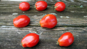 Seven red tomatoes scattered on a wooden surface