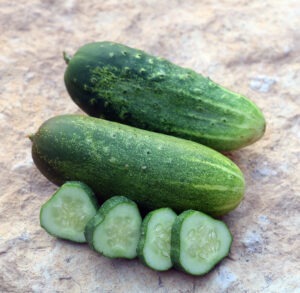 Two cucumbers lying on a rock next to four cucumber slices