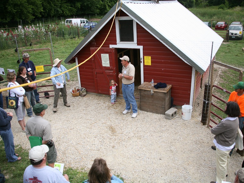 A group of people gather outside of a large red chicken coop