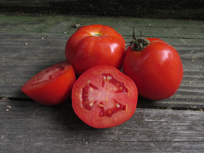Two tomatoes and two tomato halves on a wooden surface