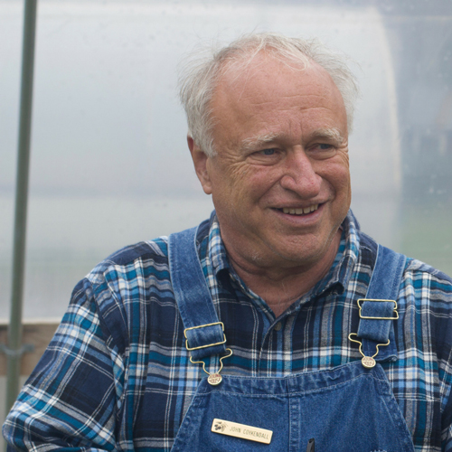 A man in overalls smiles to his left