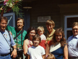 A group of adults and children stand and smile in front of a house