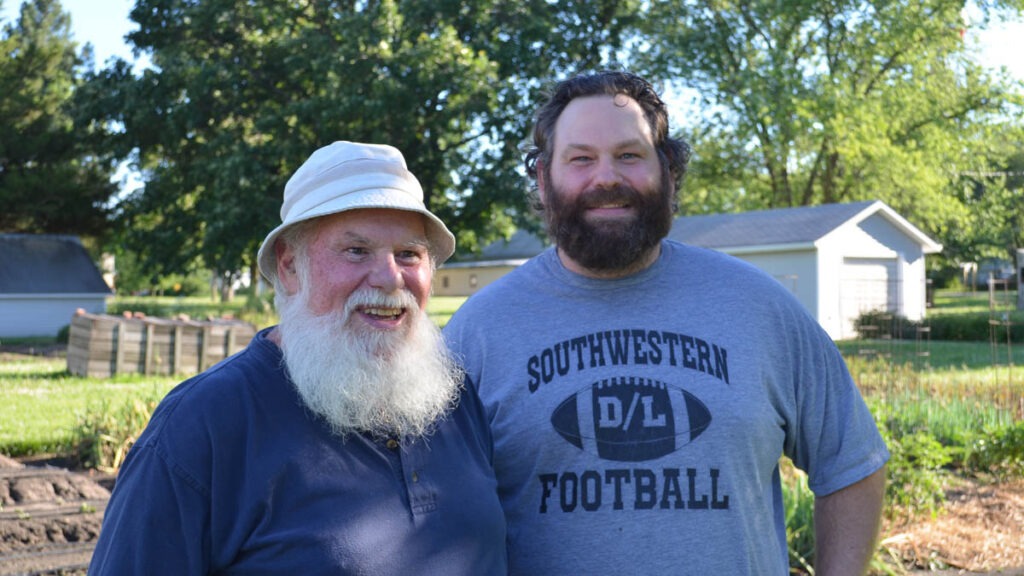 A man in a dark blue shirt and white hat and a man in a gray "Southwestern Footbal" shirt stand together outdoors