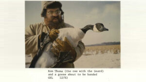 A man holds a goose in a field