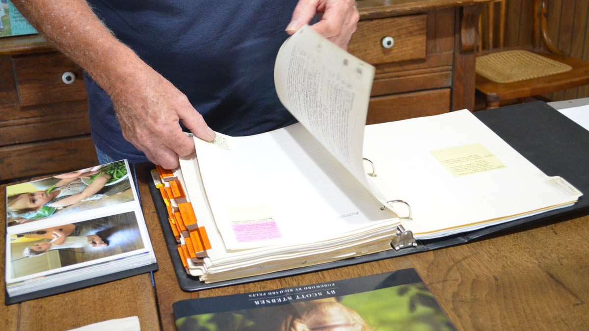 A person flips through a binder of tabbed notes on a table next to a photo album
