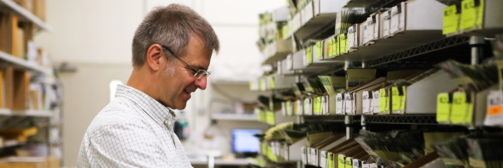 A man smiles and looks at shelves with seed packets in files