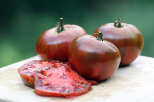 Three dark red-purple 'Paul Robeson' tomatoes with two tomato slices