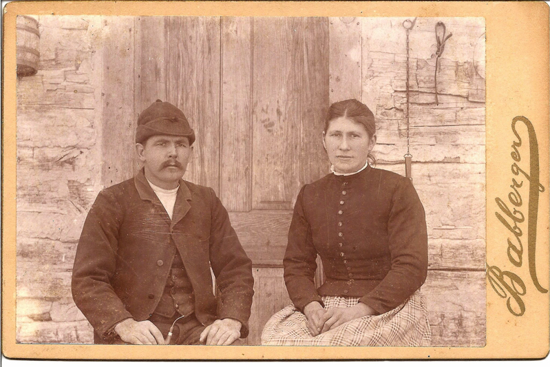 An old photo of a man and a woman seated in front of a wooden background in sepia