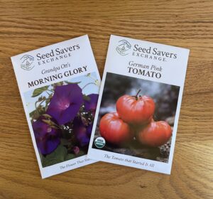 A packet of Seed Savers Exchange 'Grandpa Ott's' morning glory seeds and a packet of 'German Pink' tomato seeds on a wood table