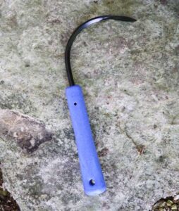 A curved hook tool with a blue handle sitting on a rock