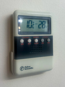 A Thermo-Hygro device on the wall with various buttons and a screen that measures room temperature and humidity. The screen reads 10° C Dry 28%