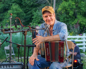 Dave Moore on stage at the 2023 Benefit Concert with an accordion on his knee. 