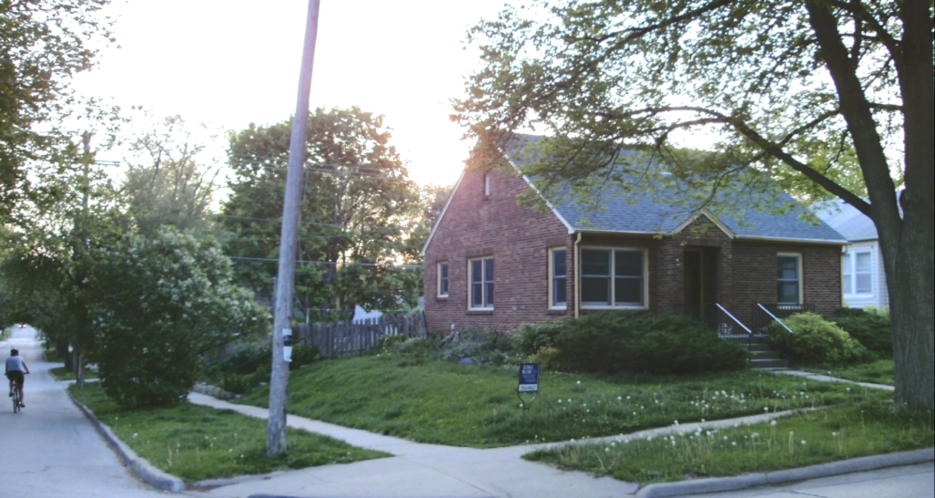 A brick house on a street corner with a green lawn and a sidewalk