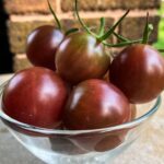 A glass bowl of small, round, deep red cherry tomatoes with short green stems