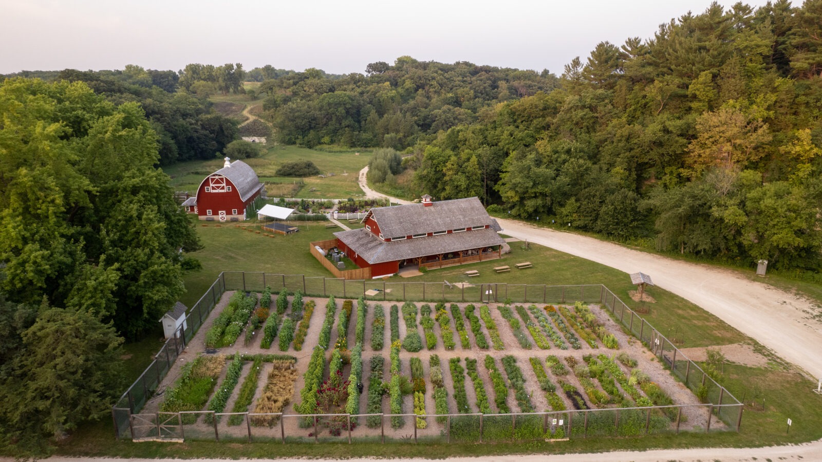 An aerial view of a farm with a large garden, red building, and red barn, surrounded by trees