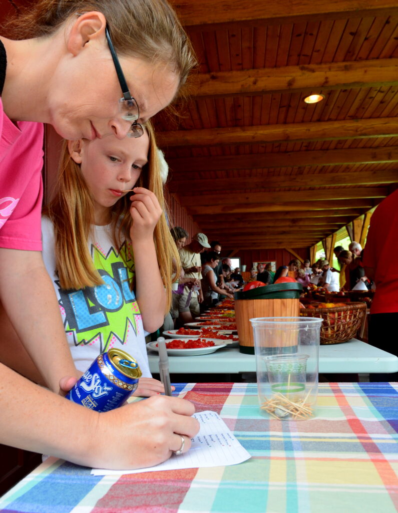 A child looks on as a woman' writes on a piece of paper.