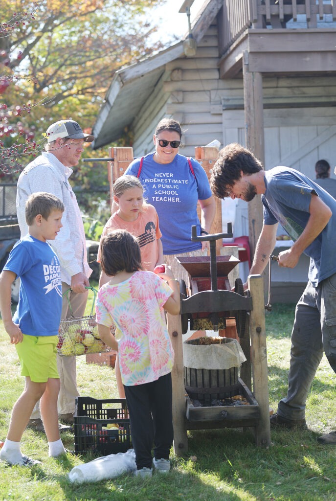 A group of people gather around an apple press.