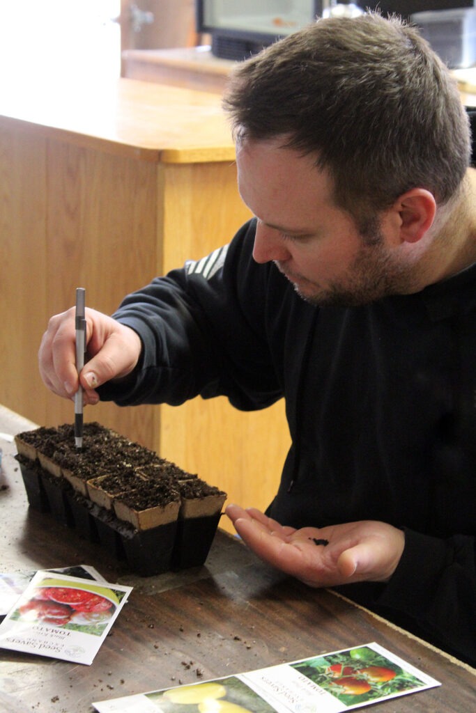 Man uses a pen to create a hole for seeds.