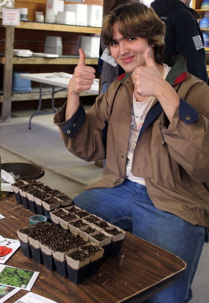 Person giving two thumbs up with several seed starts in front of them.