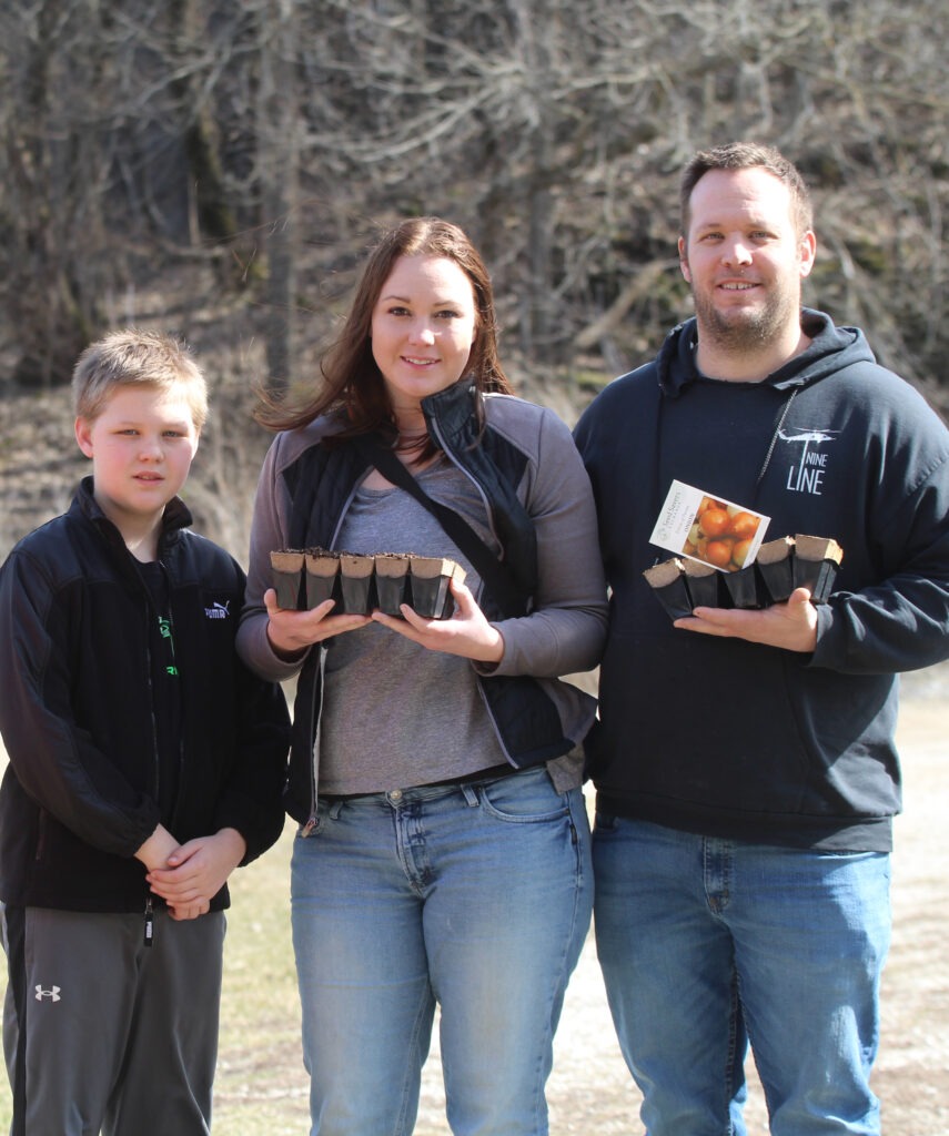 Three people smile at the camera with their seed starts.