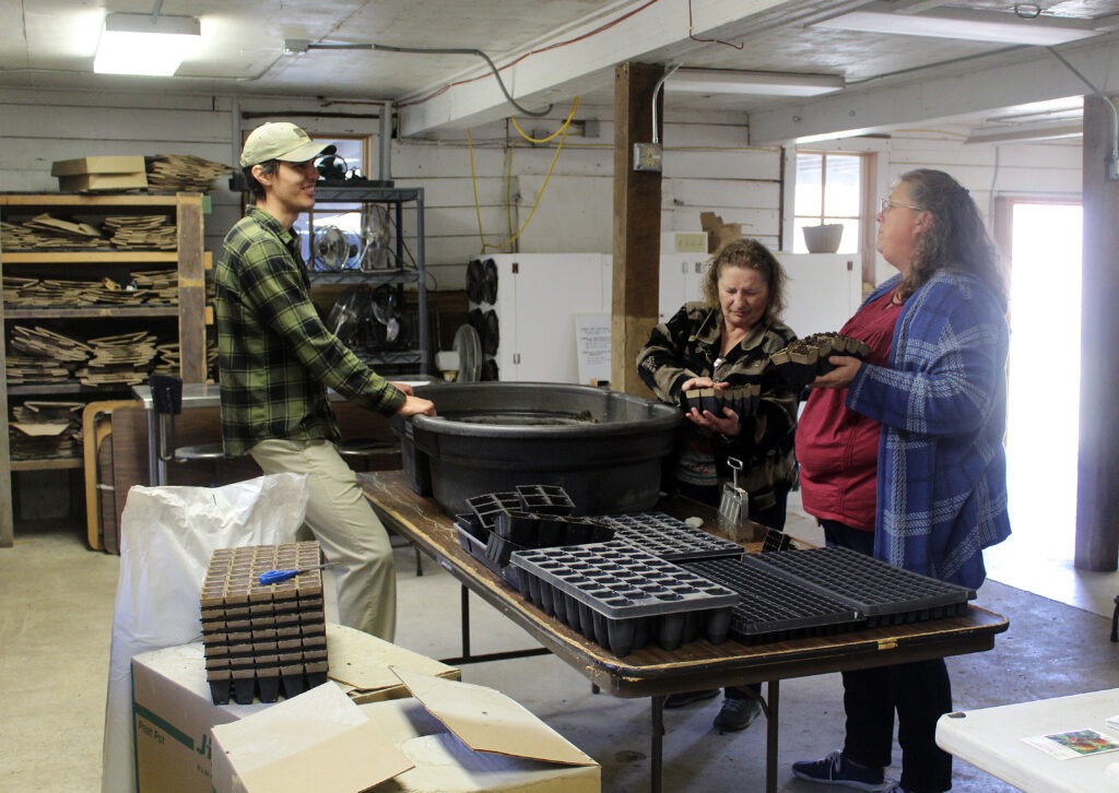 Three people stand around a table with a black tub between them.