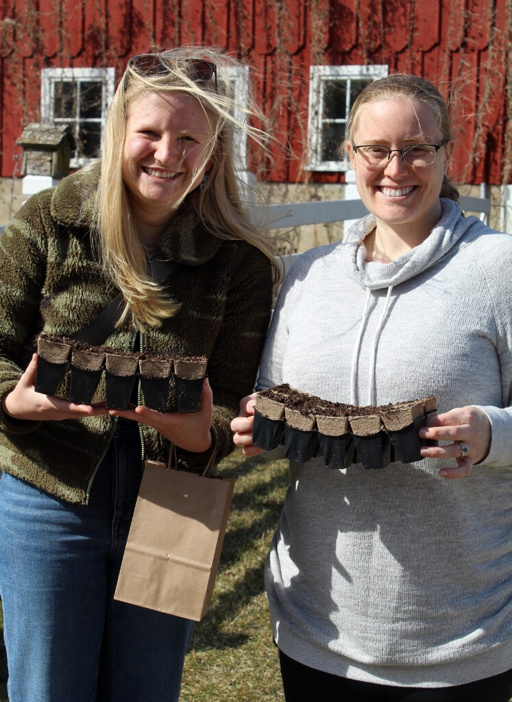 Two people smile to the camera holding seed starts.