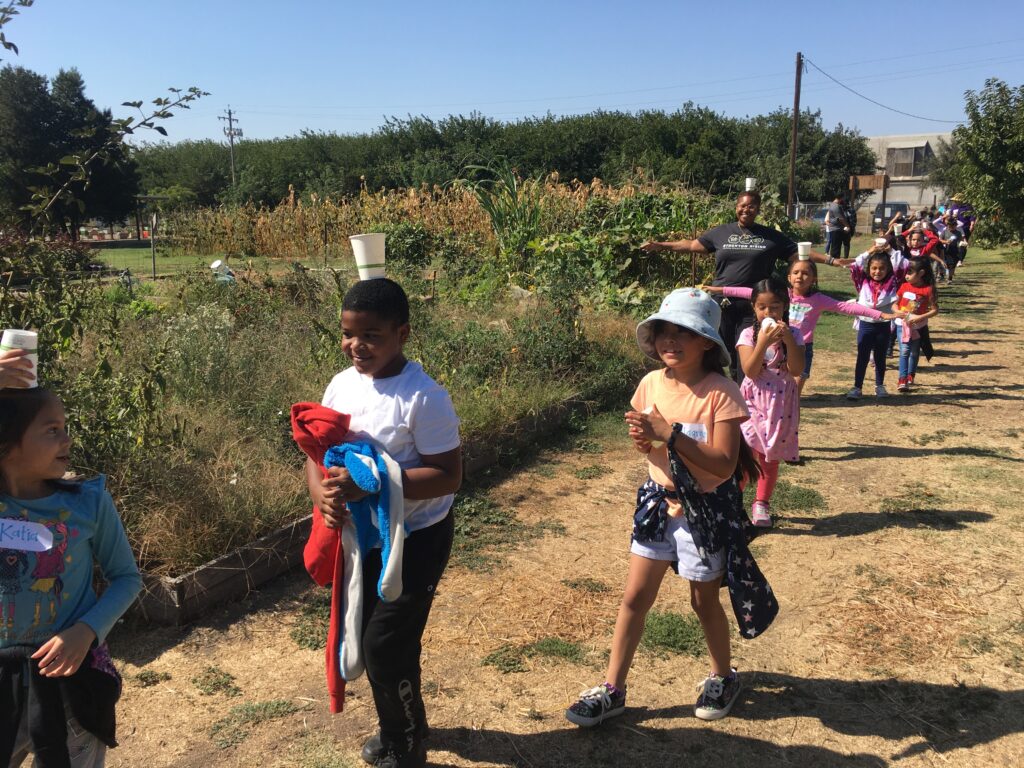 Children participating in the collard curriculum project walk through a garden while balancing cups on their heads