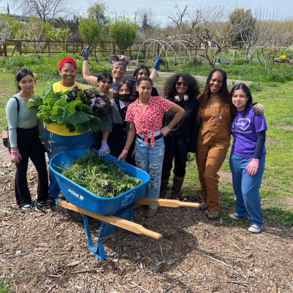 A group of middle school student participants of the collard curriculum pose with a wheelbarrow of collard greens