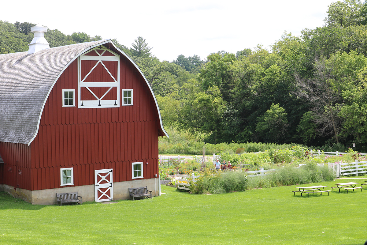 A red barn with a luscious garden next to it, surrounded by grass and trees
