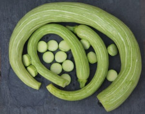 Three green-and-white striped, curved squash nestled together, with sliced squash in the middle. 