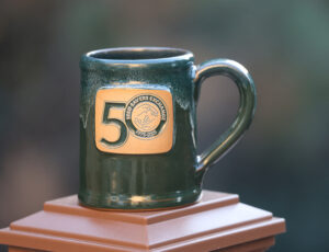 hunter-green ceramic mug bearing tan 50th-anniversary logo