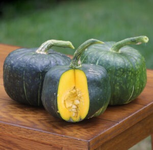 Three green squash, one with a slice taken out, sit on a wooden table