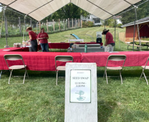 Long tables with tablecloths arranged under a large tent, with a sign in front