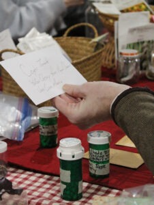 A hand holds up a notecard in front of small containers of seeds on a table