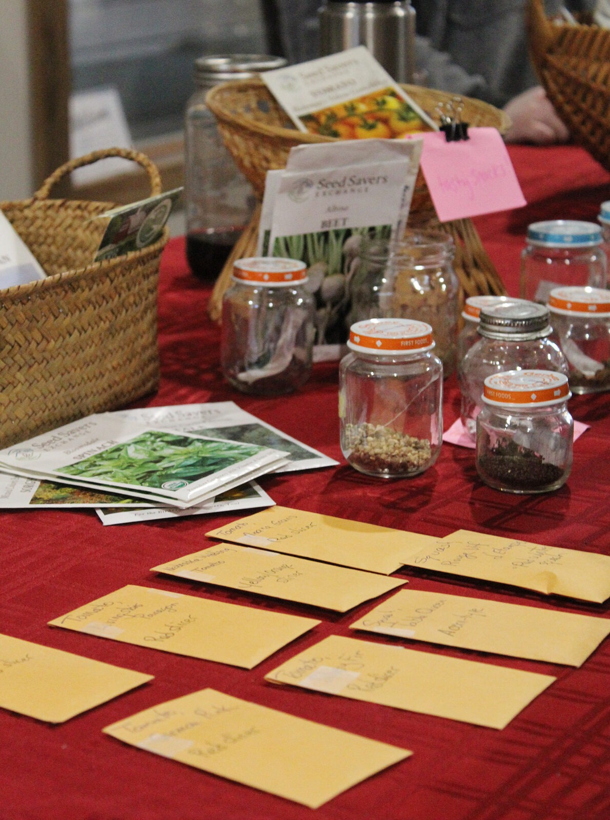 packets of seeds and small jars of seeds spread out on a red tablecloth